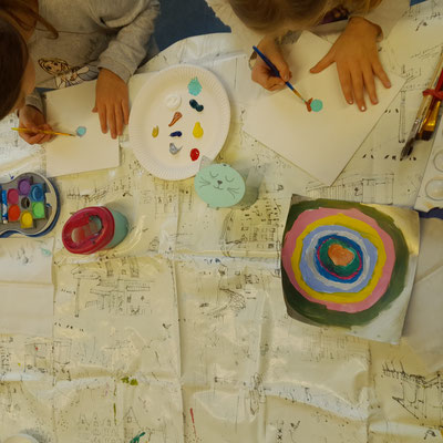 die-malerei-ag-stellt-sich-vor4 Kinder malen an einem Tisch; vor ihnen liegt ein quadratisches Bild mit farbigen konzentrischen Kreisen.