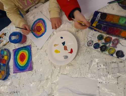 Kinder malen an mehreren kleinen Bildern mit farbigen konzentrischen Kreisen.