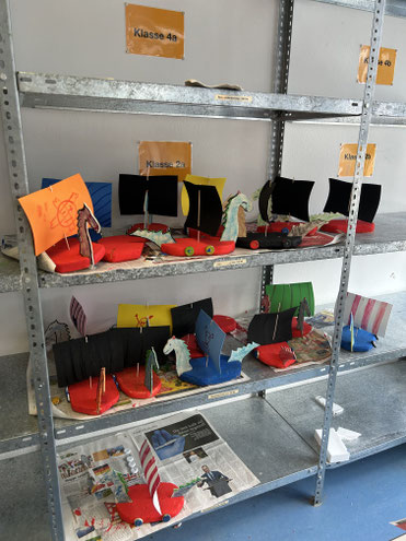 Mehrere bunte, selbstgebastelte Wikingerschiffe stehen auf einem Regal.