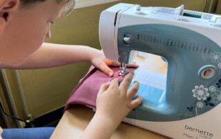 Kind näht ein rosa Stoffstück an einer Nähmaschine.