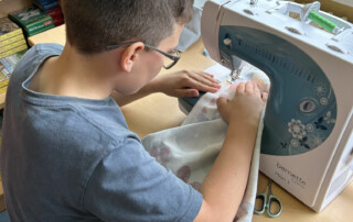 Kind positioniert ein Stoffstück an der Nähmaschine.