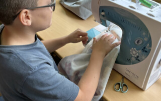 Kind steckt Stoffstücke zusammen und bereitet sie an der Nähmaschine vor.