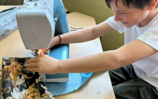 Kind näht mit einer Nähmaschine und hält den Stoff mit beiden Händen.