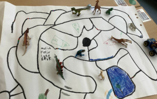 Großes Kinderbild mit einem gezeichneten Weg und kleinen Tierfiguren liegt auf einem Tisch.