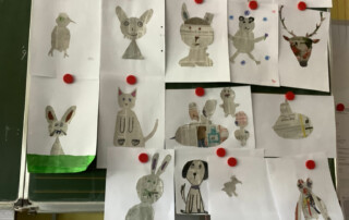 Mehrere gestaltete Papierfiguren hängen an einer Leine in einem Klassenraum.