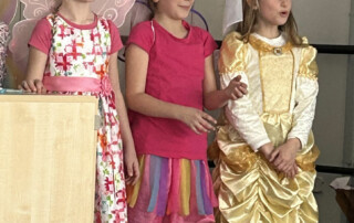 Kinder in farbenfrohen Kostümen stehen nebeneinander während einer schulischen Aufführung.